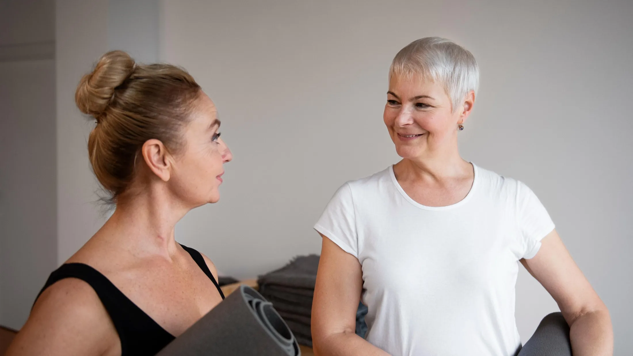 Zwei Frauen mit Gymnastikmatten im Gespräch vor dem Rehasport-Kurs